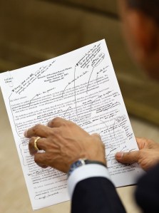 Obama holding pen and printed speech with heavily edit marks.