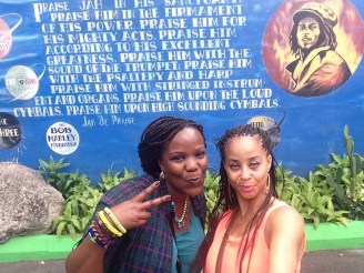 Two black women wearing braids taking a selfie in front of a Bob Marley mural